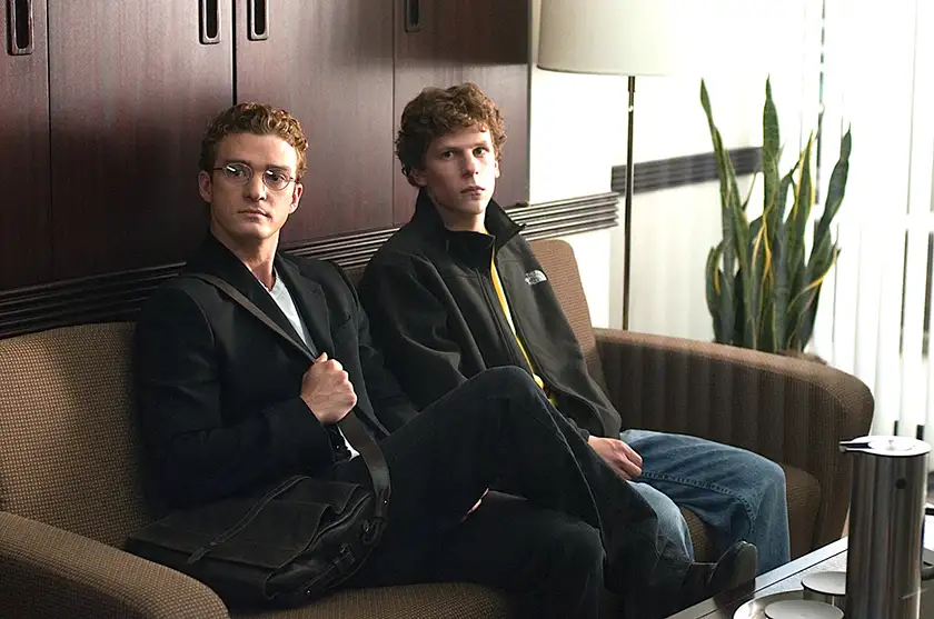 Justin Timberlake and Jesse Eisenberg sit on a chair in a waiting room in the film The Social Network