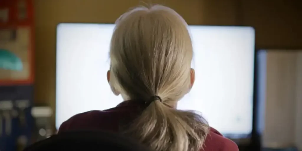 A woman with a ponytail, seen from behind, looks at a white computer screen in the film Whatever It Takes