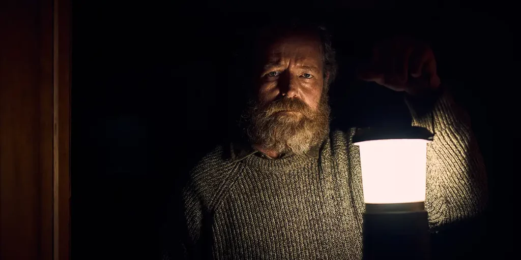 Brendan Rock as “Patrick" holds a lamp in the dark in the Shudder film You’ll Never Find Me