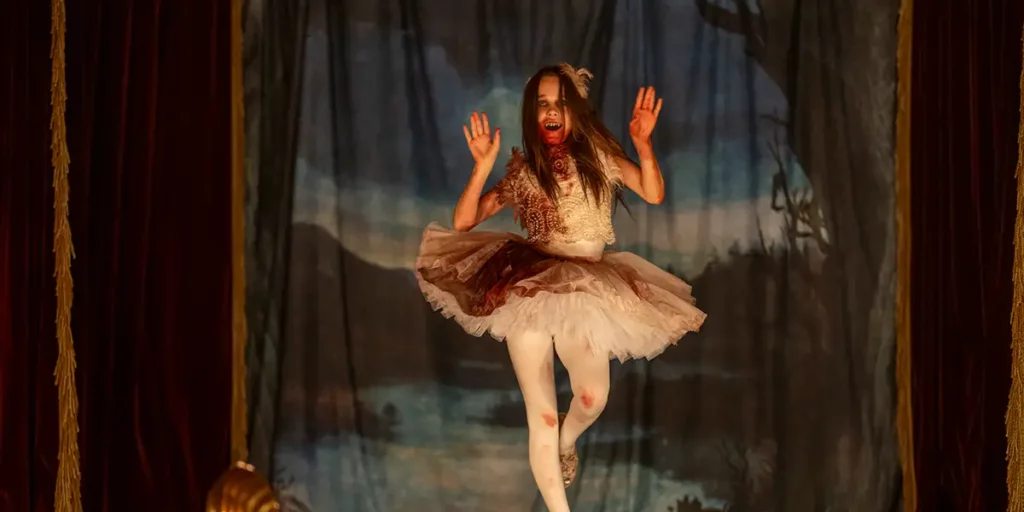 A vampire dances on a stage with a white ballerina dress soaked in blood in the film Abigail