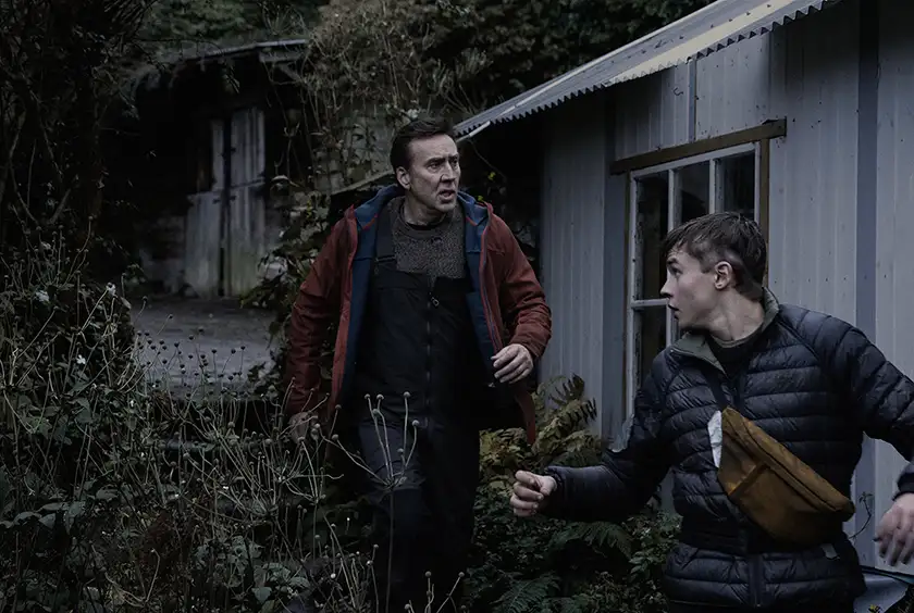 Nicolas Cage and Maxwell Jenkins walk in the garden of a house, alarmed, in the film Arcadian