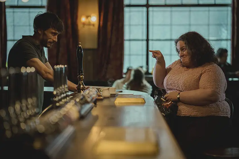 Richard Gadd as Donny is behind the bar and Jessica Gunning as Martha points at him on the other side of the counter in the Netflix series Baby Reindeer