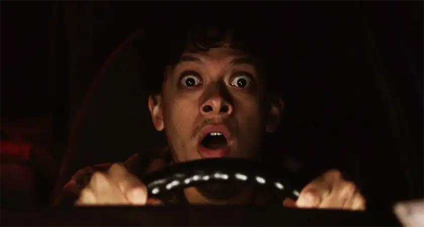 A young man looks scared while driving a car in the film Blackout