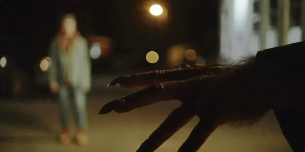 A hand of a monster is in the foreground with the figure of a woman in the background in the film Blackout