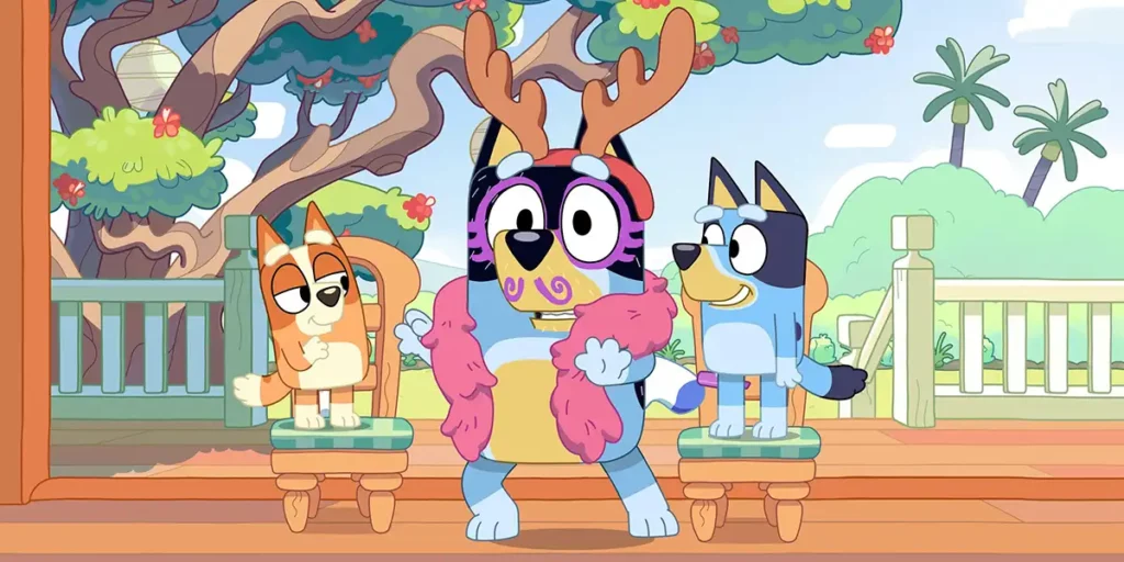 Two characters of the series Bluey stand on stools while Bandit is dressed as a reindeer