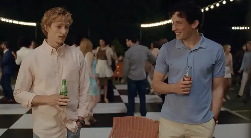 Mike Faist and Josh O'Connor drink beers wearing casual clothes at a party, looking at each other and smiling, in the film Challengers, whose perfect ending is explained in this article