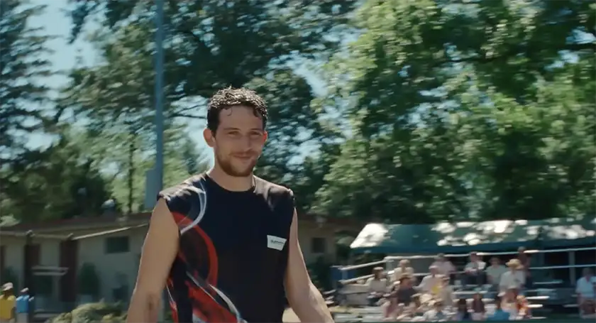 Josh O'Connor, as Patrick, wears a black tank top and smiles at someone during a tennis match in the film Challengers, whose perfect ending is explained in this article