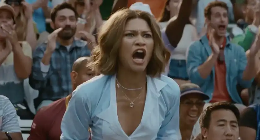 Zendaya stands up shouting at a tennis match in a crowd, wearing a smart blue shirt, in the film Challengers, whose perfect ending is explained in this article