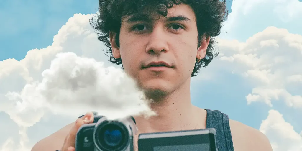 Alex holds a video camera in between clouds and looks at the camera in the film Fallen Fruit