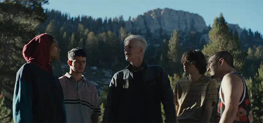 Matthew Modine and his group of cyslists stand in front of the mountains, looking at each other in a circle, in the movie Hard Miles
