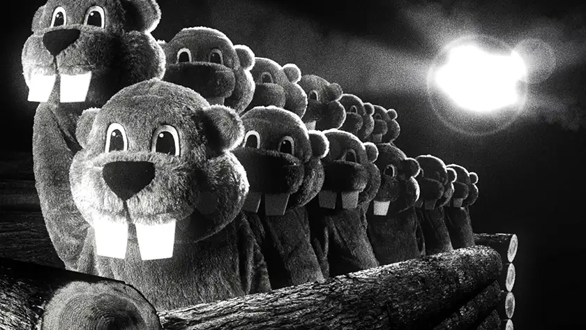 Many people wearing beaver costumes stand in line on some pieces of wood with a light behind them in the 2024 movie Hundreds of Beavers