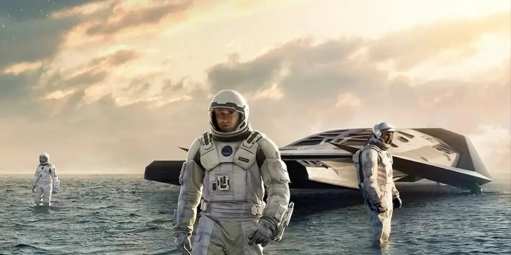 Matthew McConaughey walks in the water with a spaceship and two astronauts behind him in the movie Interstellar