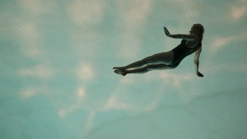 A woman floats swimming in a swimming pool, seen from below, in the film It's Not Me