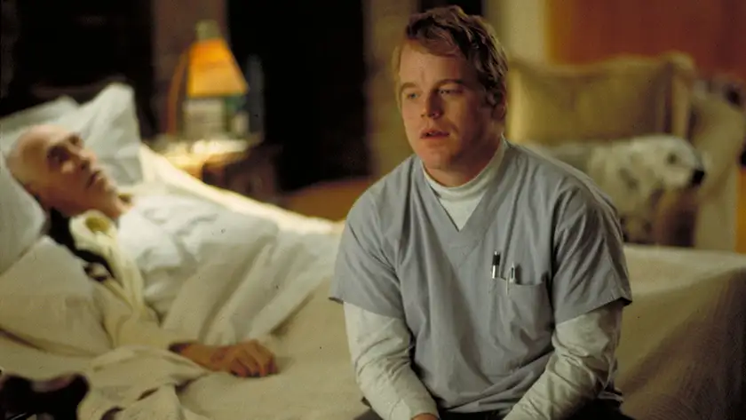 An old cancer patient lies on a bed, and a young man sits on the bed next to him, talking, in a still from the movie Magnolia, which explores the theme of hope