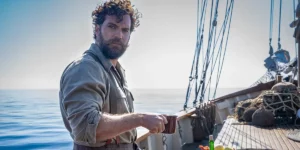 A man stands on the deck of a ship holding a copper cup in the film The Ministry of Ungentlemanly Warfare