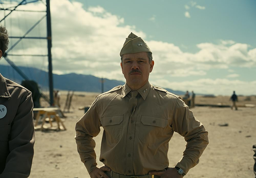 Matt Damon, a soldier wearing a uniform, stands in the middle of the desert with hands on his hip in Oppenheimer