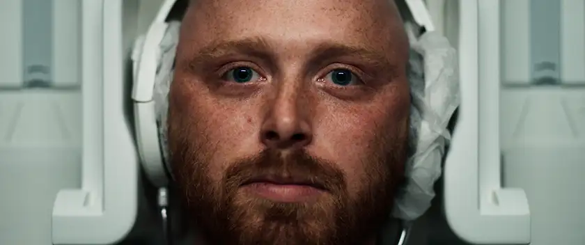 the face of a man seen from above while he's in the MRI machine during a head scan in a still from the 2024 film Red Herring