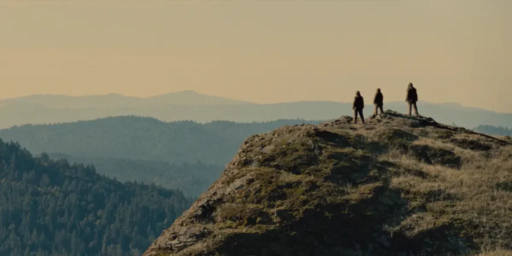 Three bigfeet are on top of a hill, looking at the mountains, in the 2024 film Sasquatch Sunset