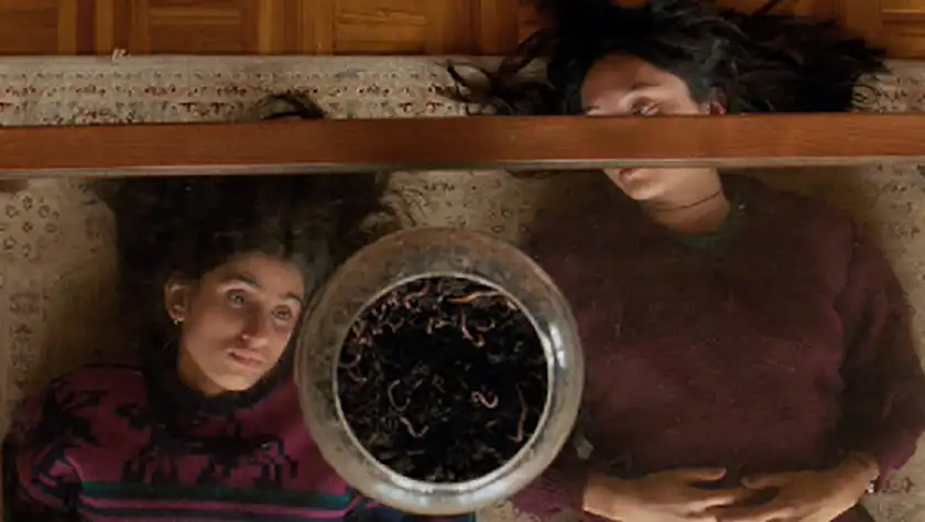 two women look at each other lying on the floor under a glass table in the film SEPTEMBER SAYS