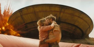 Emily Blunt and Ryan Gosling kiss each other in front of an explosion and a round building in the movie The Fall Guy