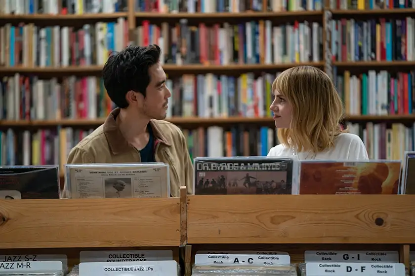 Justin Min and Lucy Boynton look at each other behind a shelf at a record store in 2024 film The Greatest Hits