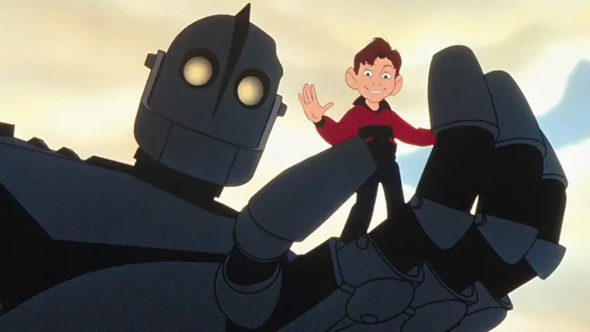 A giant robot holds a boy in his hand who is waving in the film The Iron Giant, one of the animated movies about robots recommended by Loud and Clear Reviews
