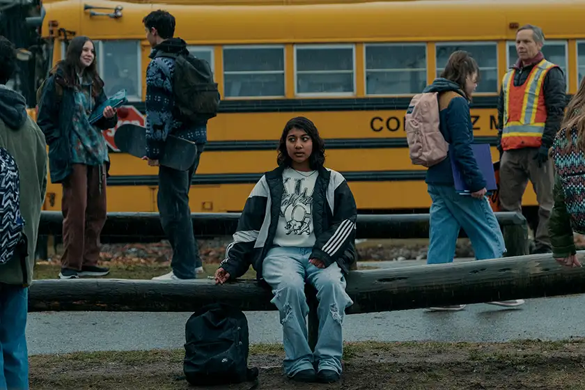 Vritika Gupta sits on a log in front of the shool bus as Reena in episodes 1 and 2 of Under the Bridge