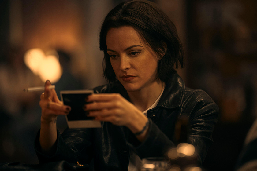Riley Keough looks at a polaroid while smoking in episode 3 of Under the Bridge