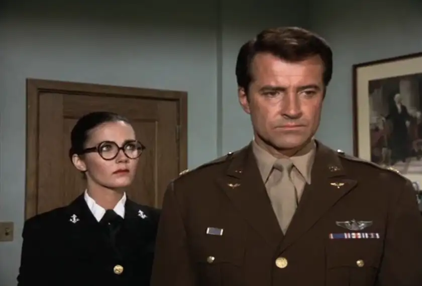 A woman wearing glasses stands behind a man in a military uniform in episode 11 of Wonder Woman (1975)
