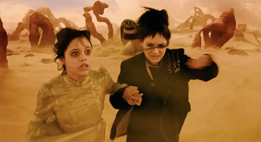 Jenna Ortega and Winona Ryder run away, terrified, in a desert, chased by a snake-like monster, in the movie Beetlejuice Beetlejuice, from an article with everything we know about Beetlejuice 2