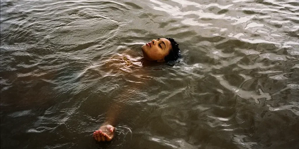 A girls lies in the water with her head pointing at the sky in the 2024 film Bird