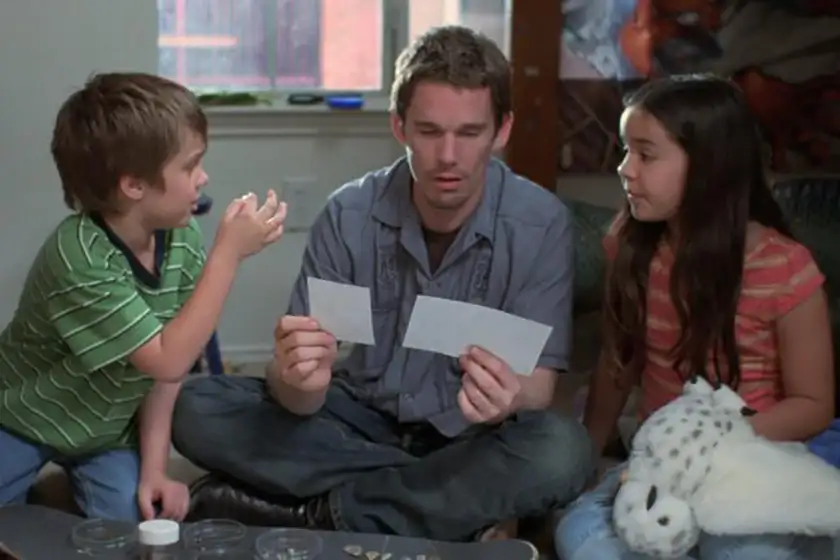 A boy and a girl sit on either site of a man who holds two pieces of paper in his hands in the Linklater film Boyhood
