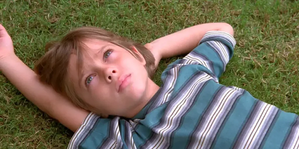A boy lies on the grass looking at the sky, wearing a striped shirt, in the Linklater film Boyhood