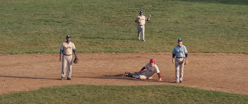 Men are on a baseball field, all looking at someone and one of them on the ground, in the film Eephus, in a photo used in the Loud and Clear interview with Carson Lund and Keith William Richards