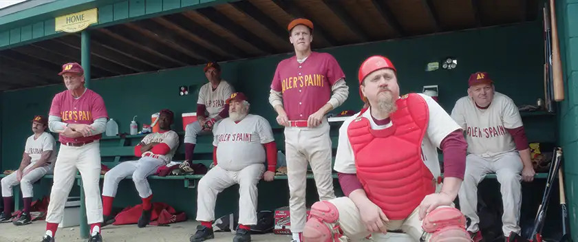 Men wearing red uniforms sit on a baseball bench in the film Eephus, in a photo used in the Loud and Clear interview with Carson Lund and Keith William Richards