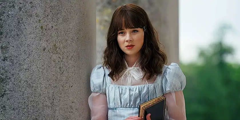 Eloise - one of the characters we can expect to see in season 3 - holds a book and looks at someone with longing in Bridgerton