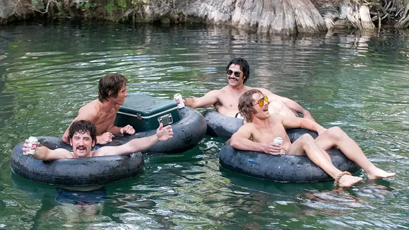 Four men sit on tires floating on a lake in the film Everybody Wants Some!!