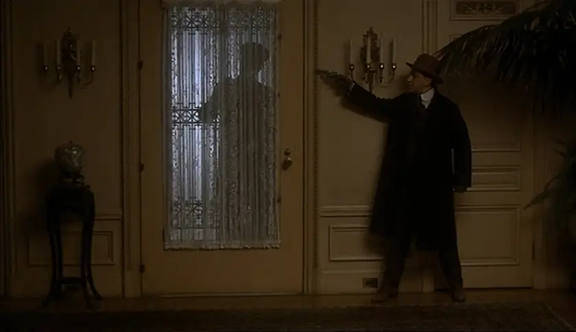 A man stands in a dark house next to a door where another man is about to come in, waiting to take him by surprise, in the film The Godfather Part II, one of all Francis Ford Coppola movies ranked from worst to best by Loud and Clear Reviews