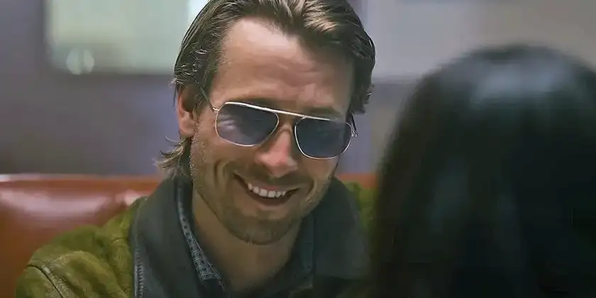 Glen Powell looks at a woman wearing Ray Ban glasses in a still from the 2024 movie Hit Man, which you need to watch