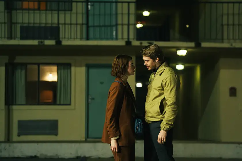 A man and a woman face each other in front of a residential building at night in the film Kinds of Kindness