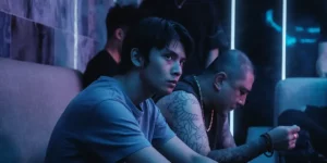 A young boy sits next to a tattooed man in the film Locust