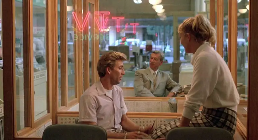 A man and a woman sit at a diner, the woman sitting on the table, in the film Peggy Sue Got Married, one of all Francis Ford Coppola movies ranked from worst to best by Loud and Clear Reviews