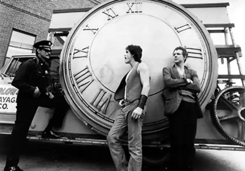 A policeman looks at two young people standing in front of a massive clock in a black and white still from the film Rumble Fish
