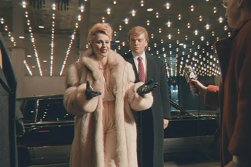 A woman with a fur coat greets a man in front of a hotel in the film The Apprentice