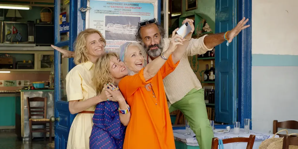 Three women and a man take a selfie in front of a restaurant in the film Two Tickets to Greece