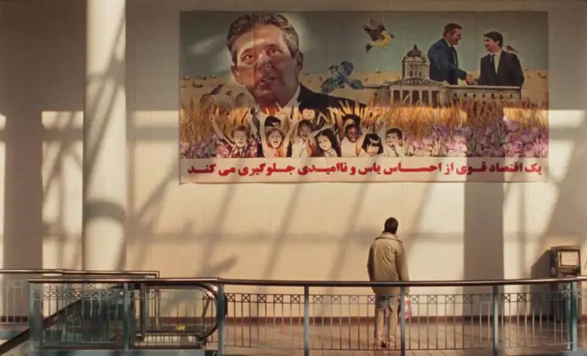 A man looks at a propaganda picture on the wall next to an escalator in the film Universal Language