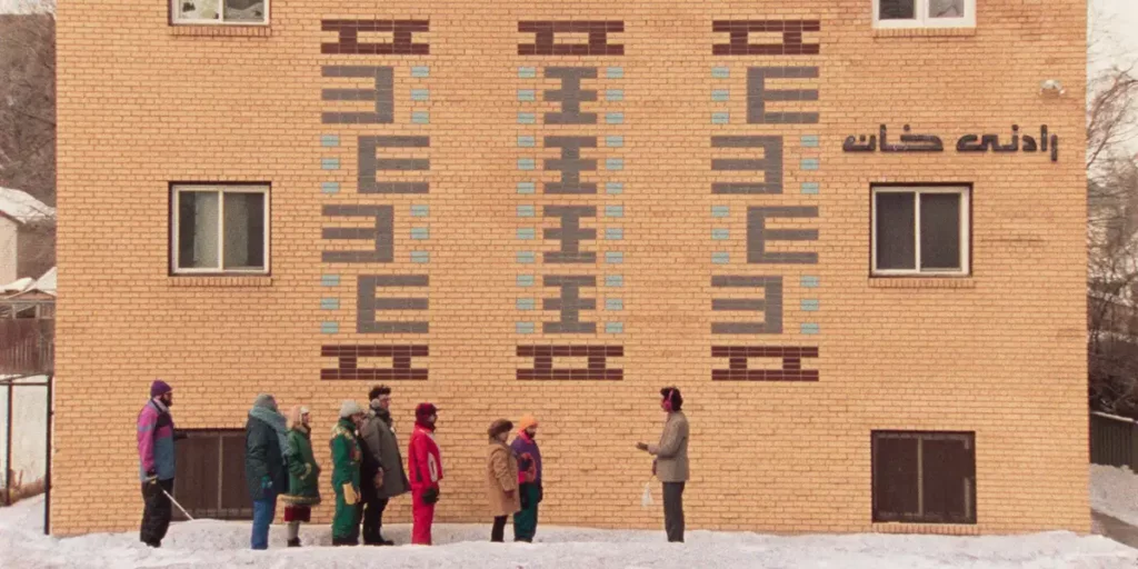 People stand in the snow talking to each other outside of an orange building in the film Universal Language