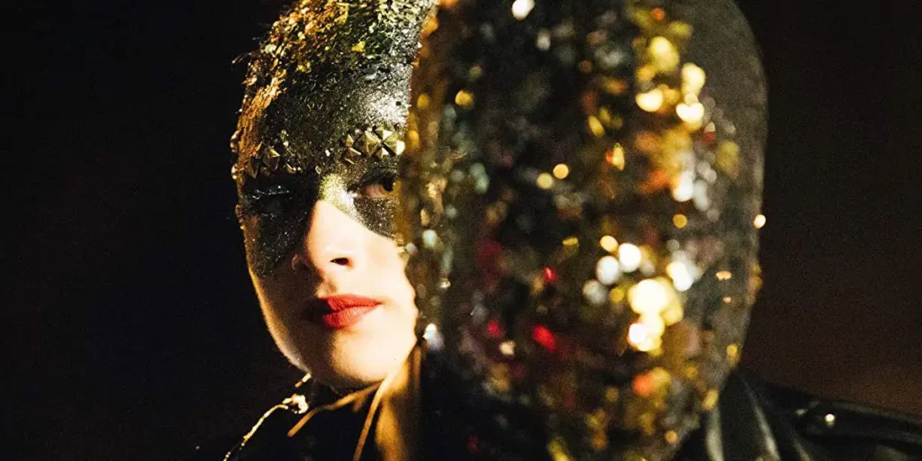 A woman wears a sparkling gold outfit that covers her head and eyes in a still from Vox Lux