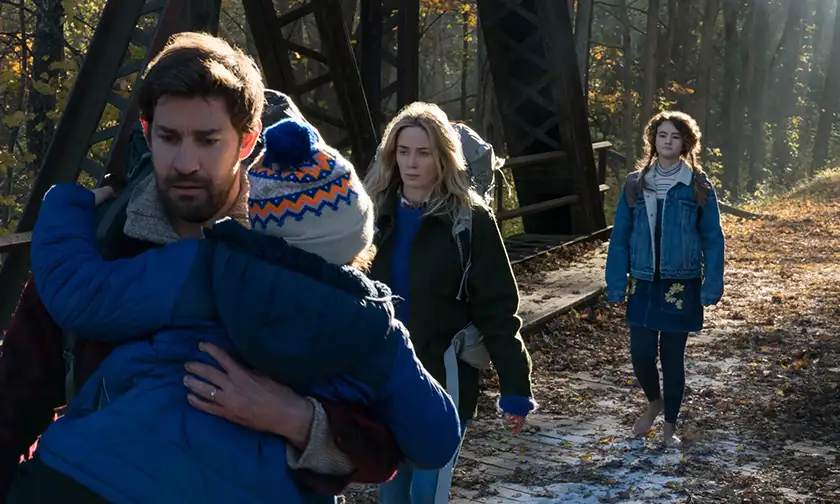 Three people walk in a park, one of them holding a child, in the 2018 film A Quiet Place