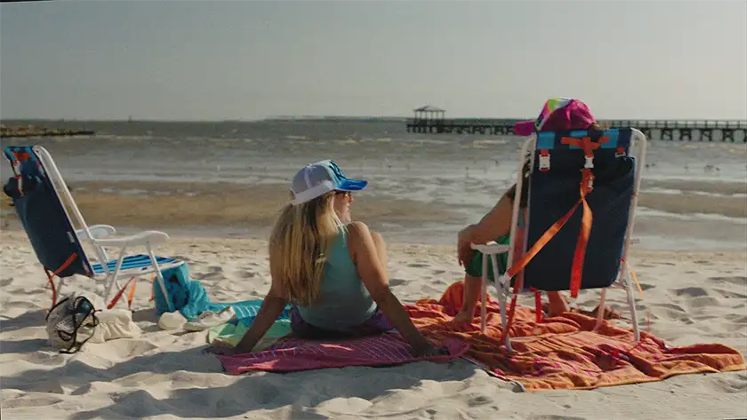 Two women sit on the beach by the sea in the film Adult Best Friend, in a photo featured on the Loud and Clear interview with Delaney Buffett and Katie Corwin